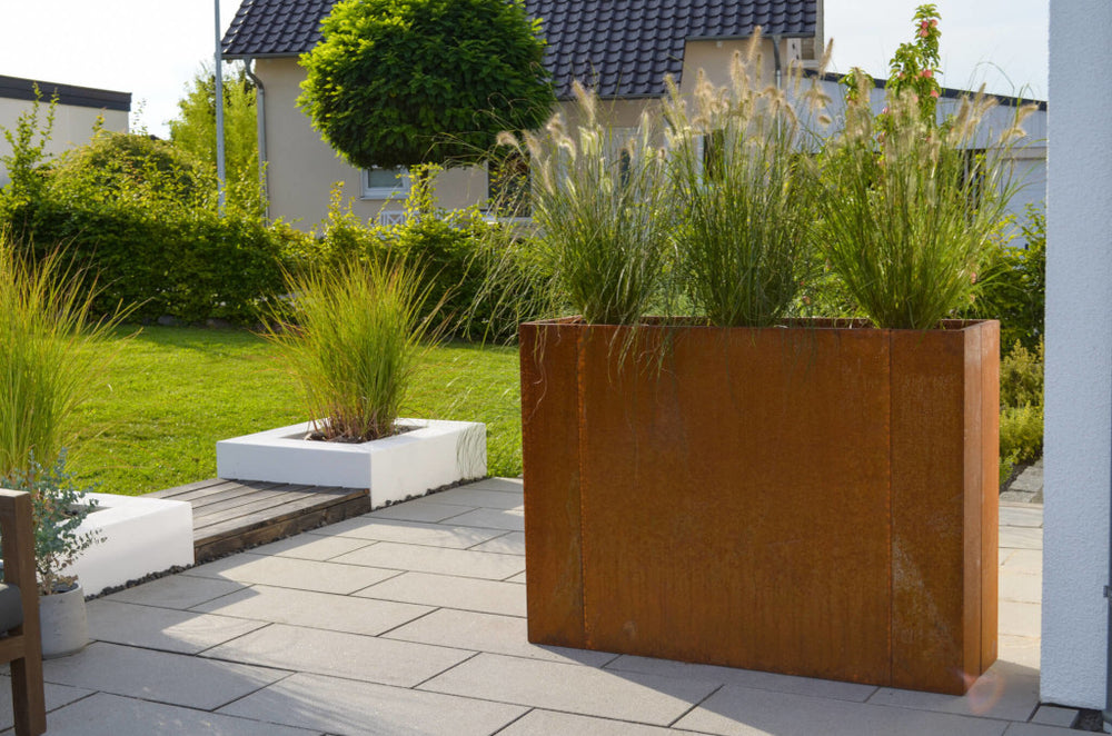 Hochbeet Manarola 40x136x100 in Cortenstahl bepflanzt auf einer Terrasse vor einem grünen Garten